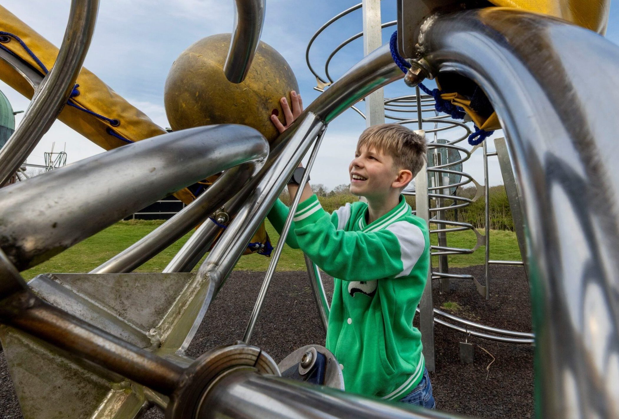 A boy wearing a green top is inside an amazing playground construction that has swooping metal bars and round balls representing planets